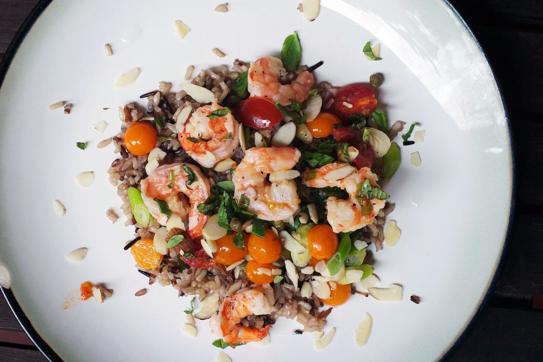 Lemon Shrimp, Capers, halved cherry tomatoes with sliced green onions over wild rice. Almond and Parmesan cheese garnish. top view.