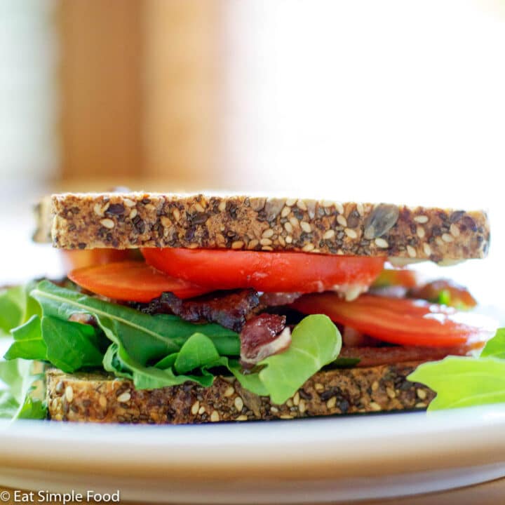 Bacon Arugula Tomato Stacked Sandwich on white plate. side view.