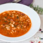 Side View of 13 bean soup in a red tomato sauce on a white wood table. side view. white bowl. Thyme sprigs in the back ground