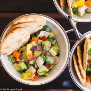Top view of a small white bowl of ceviche (diced white fish, red onions, yellow and red peppers, lime juice, and cilantro) with 3 crackers sticking out of bowl.
