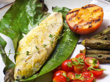 Baked Amberjack White Fish with Thyme Laying On a Green Banana Leaf On A Wood Plate