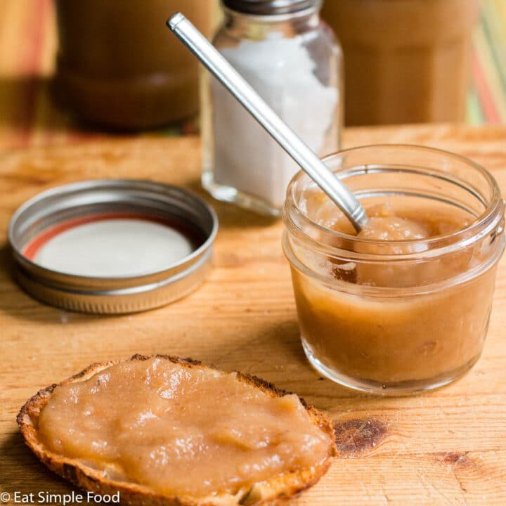 Applesauce in small jar and slathered on toast on cutting board. Side view.