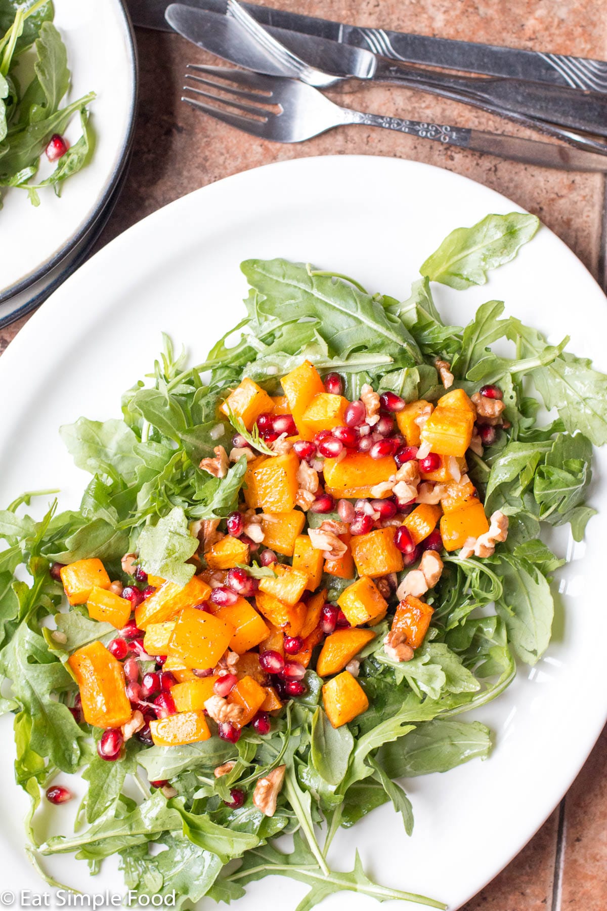 Roasted butternut squash on top of arugula on a white plate. Garnished with chopped walnuts and red pomegranate kernels. Top view.