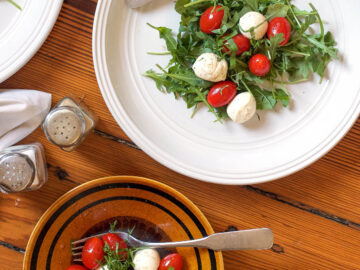 Arugula Salad topped with small mozzarella balls and cherry tomatoes on two white plates with knife and fork and salt and pepper shakers. top view.