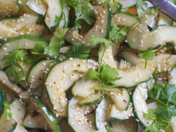 Close up of halved cucumbers with seeds taken out tossed in a soy / sesame oil sauce and topped with sesame seeds and cilantro.