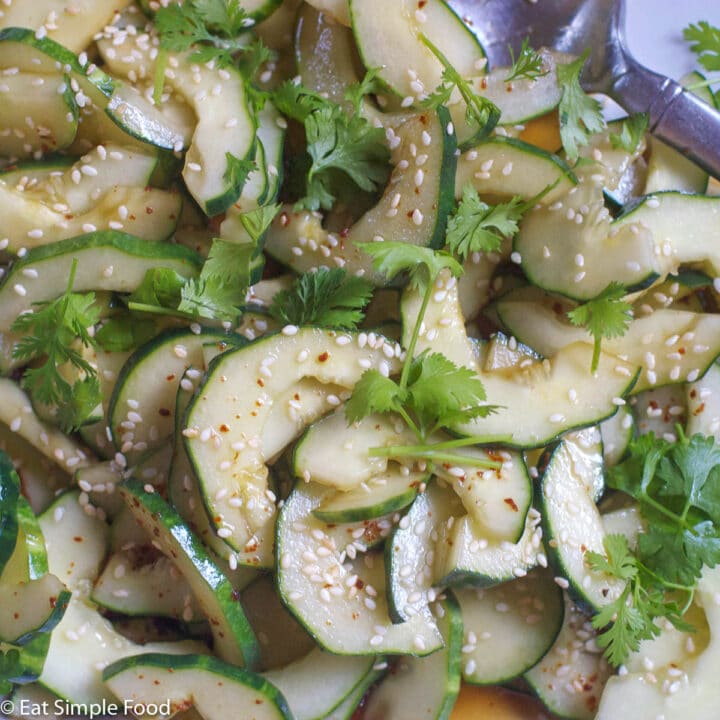 Close up of halved cucumbers with seeds taken out tossed in a soy / sesame oil sauce and topped with sesame seeds and cilantro.