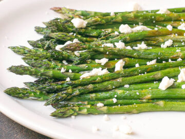 Roasted Asparagus with Feta garnish on a white plate with a black rim. side view.