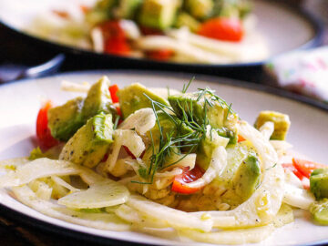2 white plates with thin sliced fennel, chunks of avocado and quartered cherry tomato salad