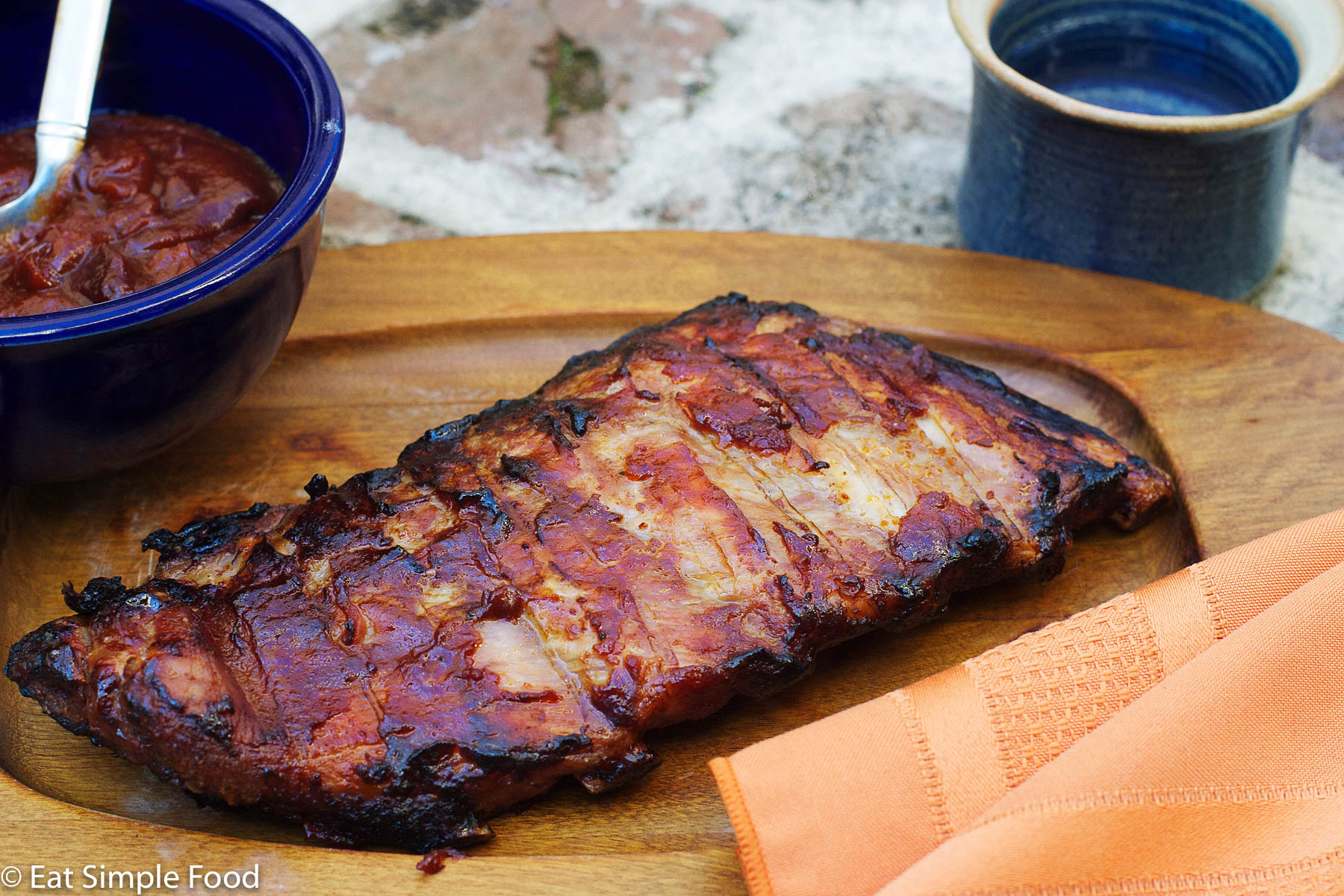 St. Louis Ribs Baked In BBQ sauce on a wood plate with an orange napkin.