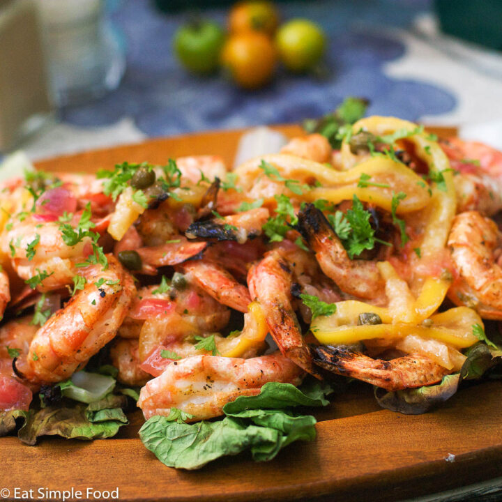 Wood plate full of BBQ Shrimp with a Lemon Garlic Sauce over a bed of greens.