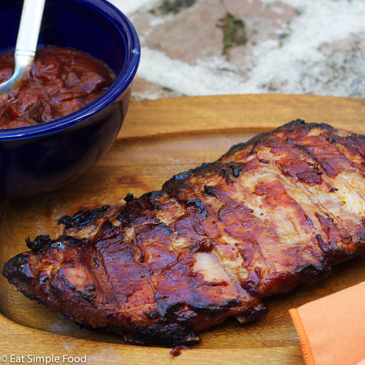 St. Louis Ribs Baked In BBQ sauce on a wood plate with an orange napkin.