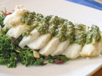 Baked Flaky Cod Fish on a bed of kale greens with a fresh dill and brazil nut pesto garnish.