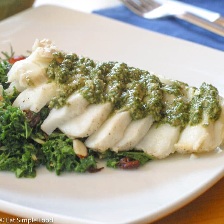 Baked Flaky Cod Fish on a bed of kale greens with a fresh dill and brazil nut pesto garnish.