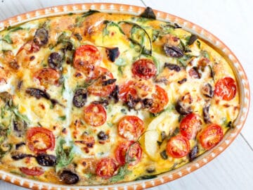 Baked Mediterranean Frittata in Oval Baking Pan with cherry tomatoes, spinach, eggs, feta, capers, and olives