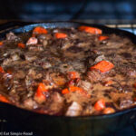 A Cast Iron Skillet over a gas oven cooking with chunked beef and carrots in a brown dark red wine gravy.