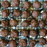 Baked Meatballs elevated on a wire rack above an aluminum lined baking sheet.