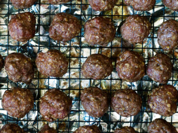 Baked Meatballs elevated on a wire rack above an aluminum lined baking sheet.