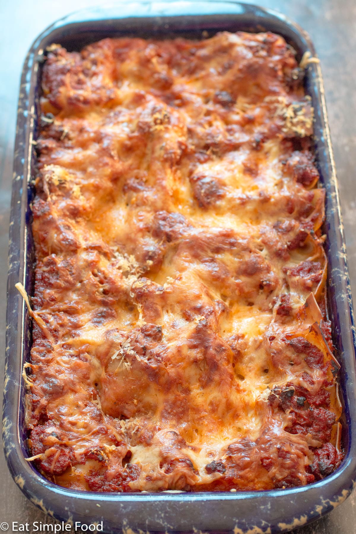 Beef and Sausage Lasagna cooked layered with melted mozzarella and Parmesan cheese in a rectangle blue baking dish.