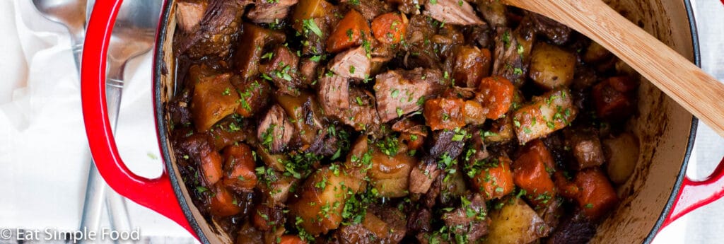 Beef, Carrots, Leeks, Potatoes cooked in a red dutch oven pot with a brown gravy. Top view.