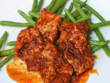 Sliced Pork in a red sauce over a bed of green beans on a white plate. Close up and side view.