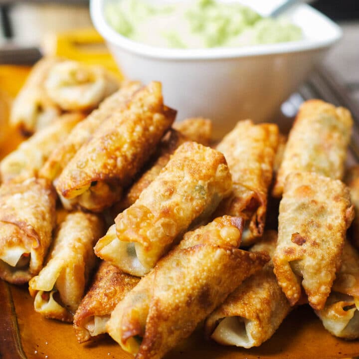 Stacked & Fried Eggrolls On a Tan Plate with a white blow of guacamole. side view.