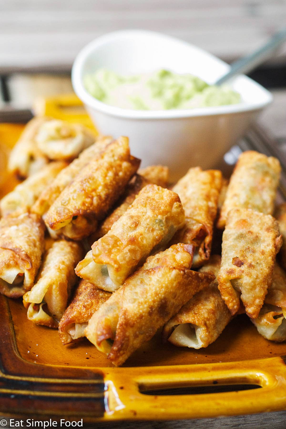 Stacked & Fried Eggrolls On a Tan Plate with a white blow of guacamole. side view.