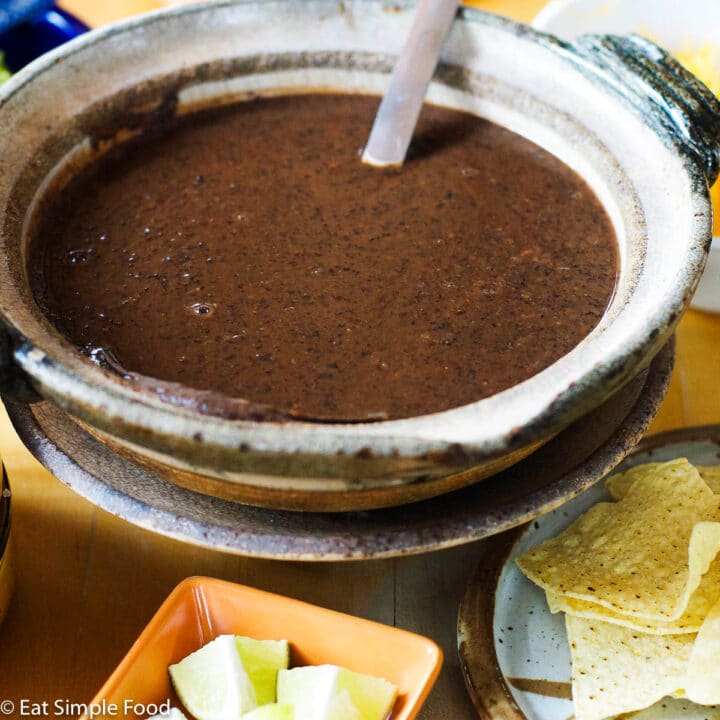 Pureed Black Bean Soup In a Brown Bowl (Side Angle) with A spoon with an orange container of lime wedges.
