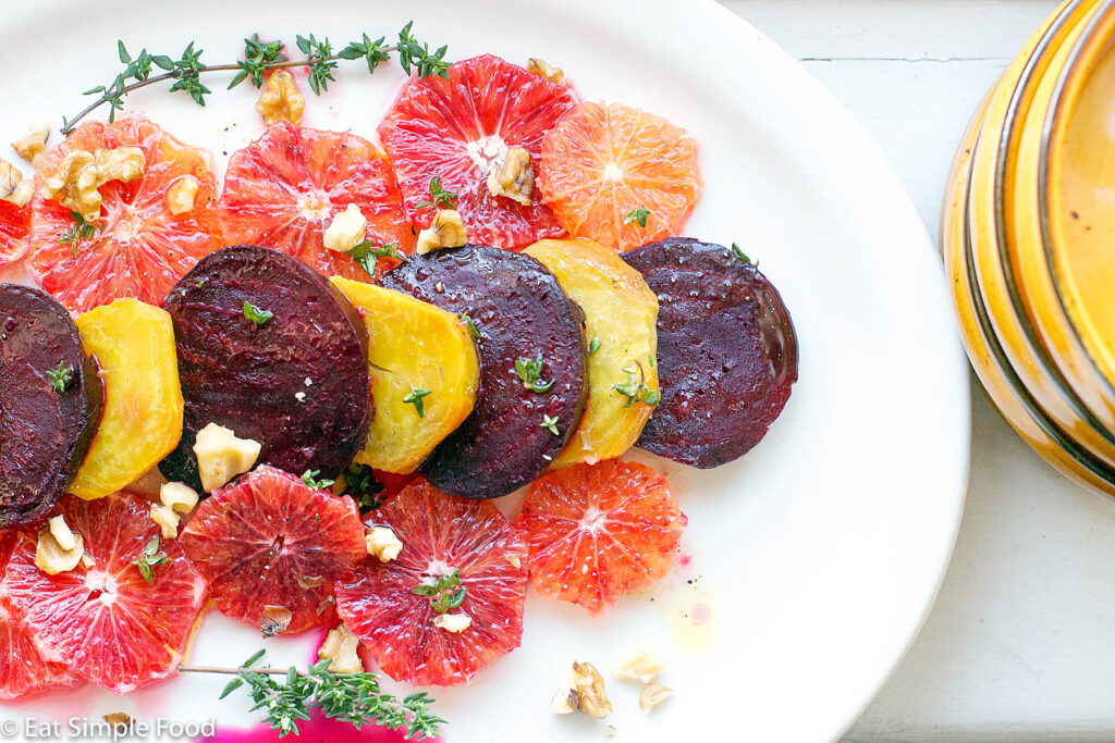 Blood Oranges & Roasted Yellow and Red Beets on a white plate with thyme and walnuts sprinkled over the top.