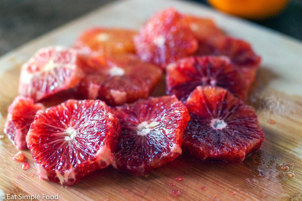 Peeled & Sliced Blood Oranges on a wood cutting board sitting in their juice.
