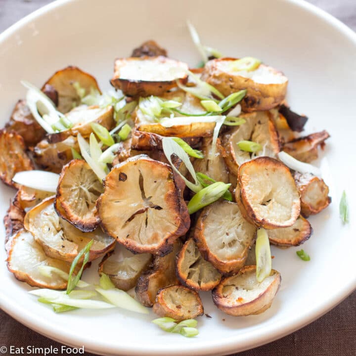 Sliced Roasted Sunchokes (Jerusalem Artichokes) On A White Plate With Green Onion Garnish