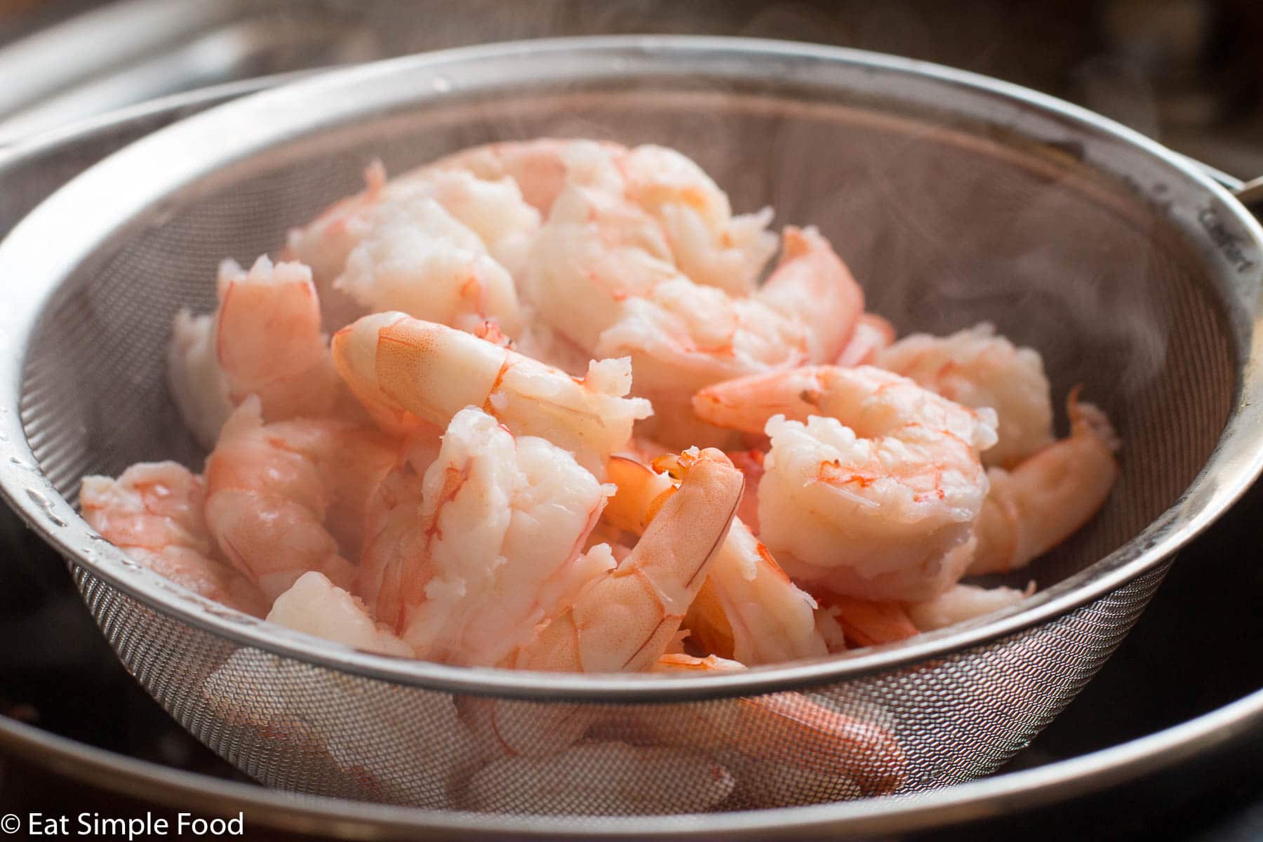 Close up of round strainer over a boil of steaming cooked peeled and deveined shrimp.