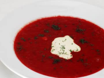 White bowl of vibrant red beet soup (Borscht) with a dollop of sour cream and fresh chopped dill.