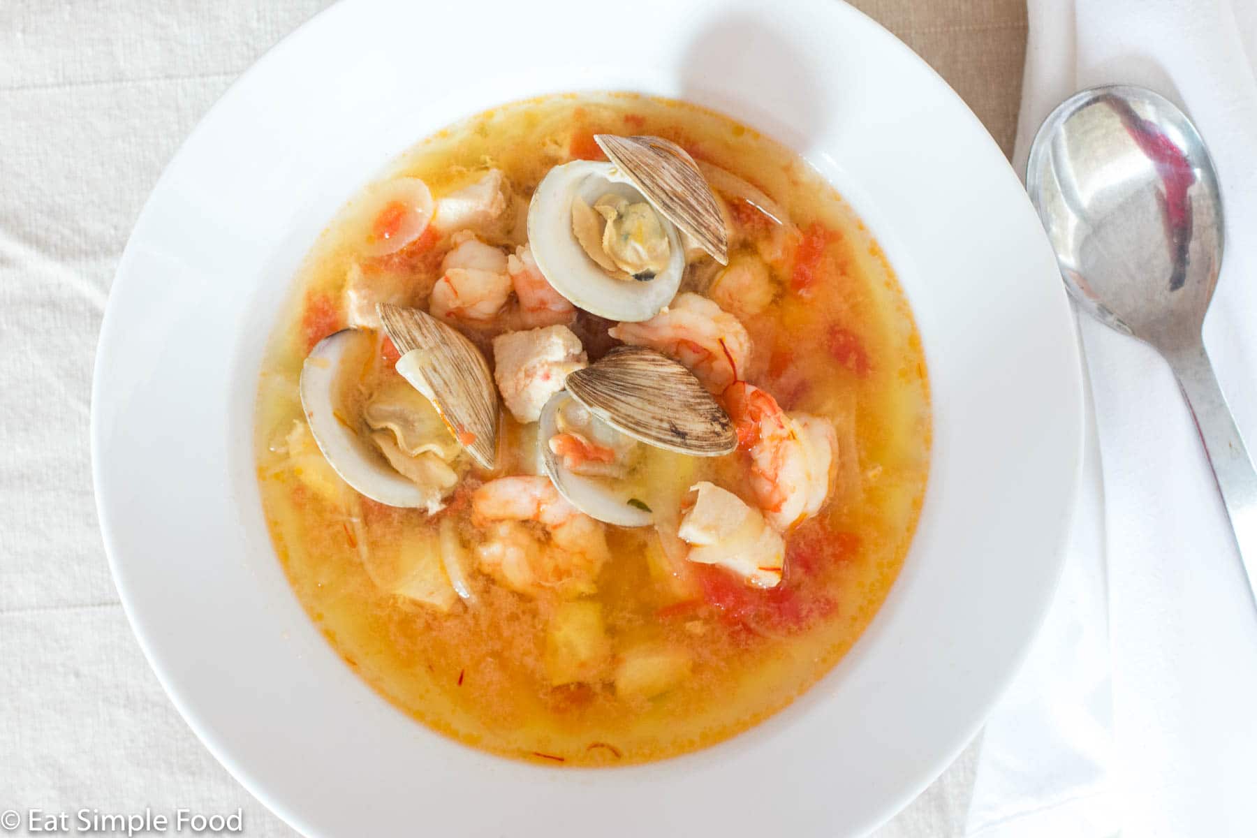 Bouillabaisse (Fish or Seafood Stew) In a white bowl with clams, shrimp, and chunks of white fish in a yellow red delicate sauce. Close up.