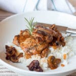 Braised Chicken & Mushrooms on a white plate, with brown gravy over rice with a thyme sprig on top.