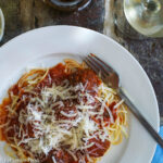 White plate of meatballs with red sauce and spaghetti with grated parmesan cheese and a fork.