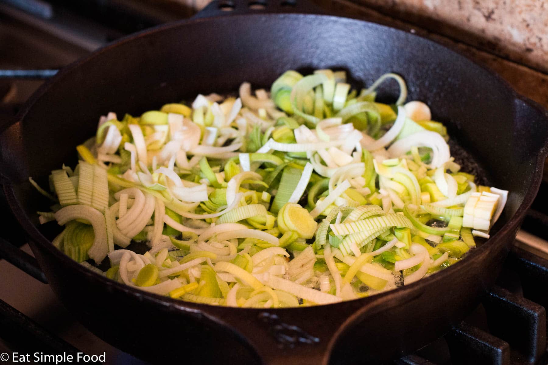 Sliced Leeks Cooking in a cast iron skillet over a gas range. side view