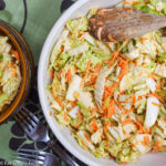 Top view of a bowl of cole slaw: cabbage and grated carrots in a white bowl. Forks on the side.