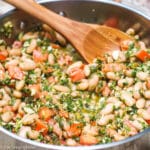 Stainless steel deep skillet filled with white beans and diced tomatoes with a lightly pulsed pesto of kale and almonds.