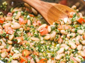 Stainless steel deep skillet filled with white beans and diced tomatoes with a lightly pulsed pesto of kale and almonds.