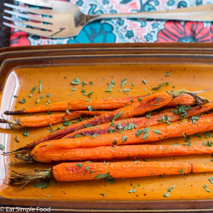 Roasted Whole Carrots on A Tan Pan with the green tops of the carrots chopped and used as a garnish