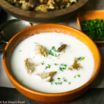 Side View wood bowl of white cauliflower soup with 5 croutons and a chopped parsley garnish