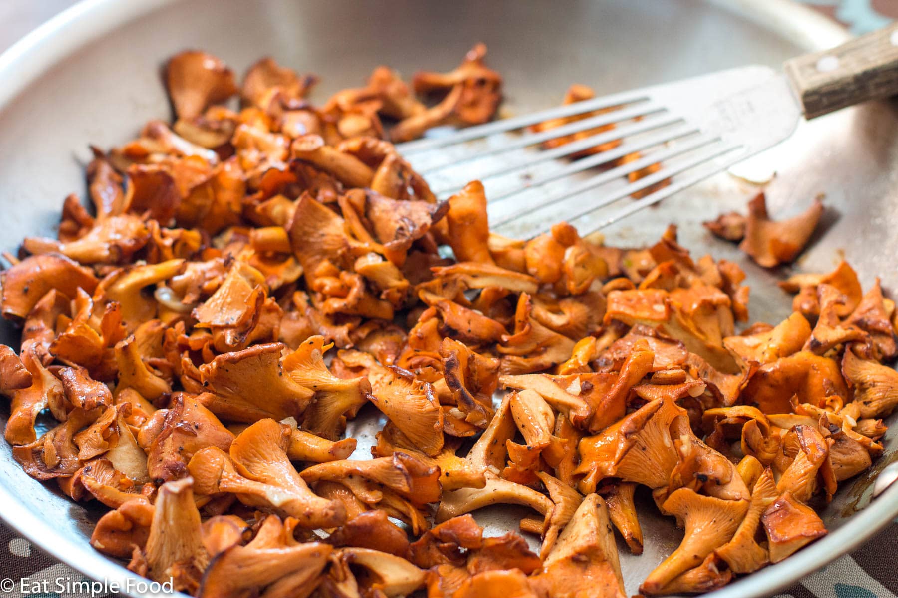 Cooked quartered orange brown chanterelle mushrooms in a stainless steel pan with a fish spatula.