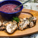 Pan Fried Chicken Thigh with a blue bowl of Grape sauce on a Wood Serving Plate with a sprig of rosemary