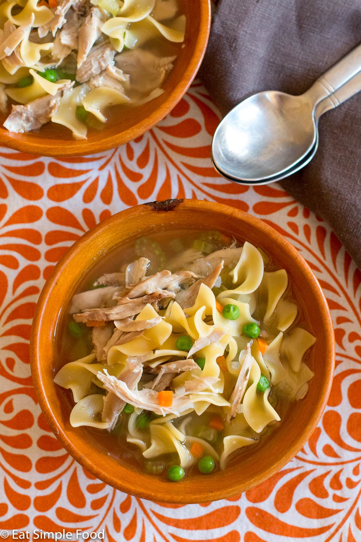 Top view of wood bowl of chicken soup with egg noodles, carrots, and peas.