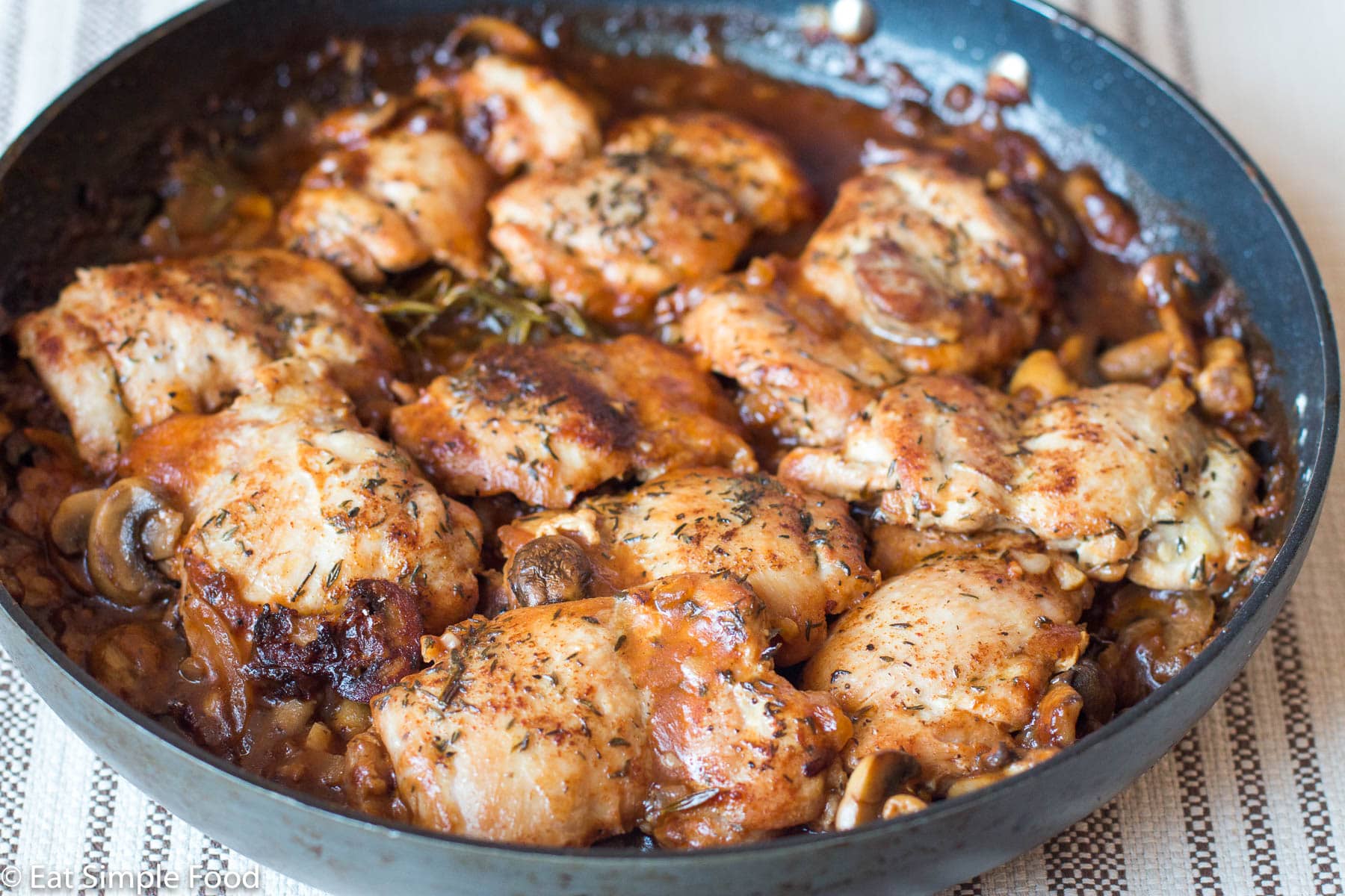 Black pan of Chicken Thighs seared brown and with a brown mushroom gravy with thyme. close up, side view