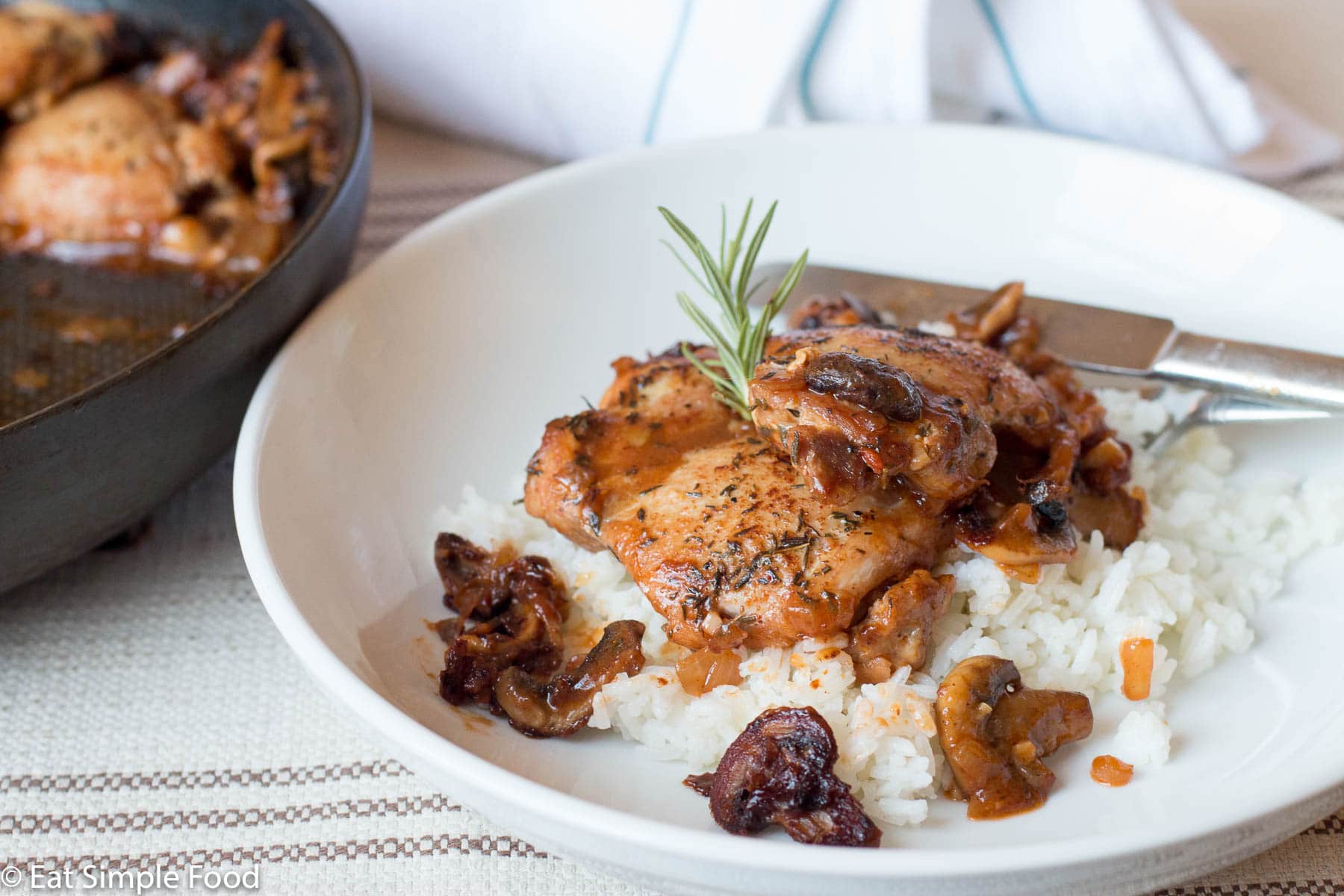 Braised Chicken & Mushrooms on a white plate, with brown gravy over rice with a thyme sprig on top.