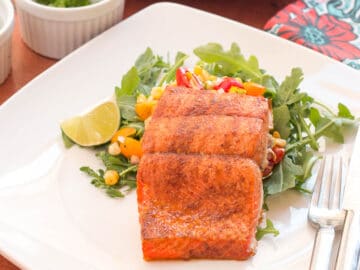 1 piece of salmon spiced with lime, paprika, and cumin on a bed of greens on a white plate