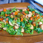 Wood oval plate with crispy romaine lettuce with cooked chicken, sliced almonds, diced carrots, celery, onions, garlic, and ginger.