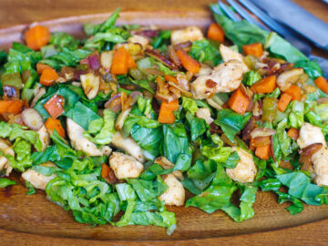 Wood oval plate with crispy romaine lettuce with cooked chicken, sliced almonds, diced carrots, celery, onions, garlic, and ginger.
