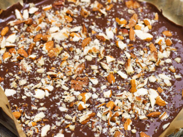 A Tart pan lined with parchment paper with homemade chocolate in it with lots of nuts.